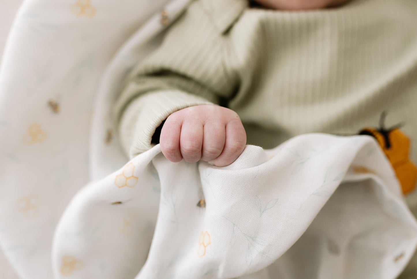 Close-up of a baby's hand holding a soft, white organic muslin in Nestle and Blooms' exclusive print