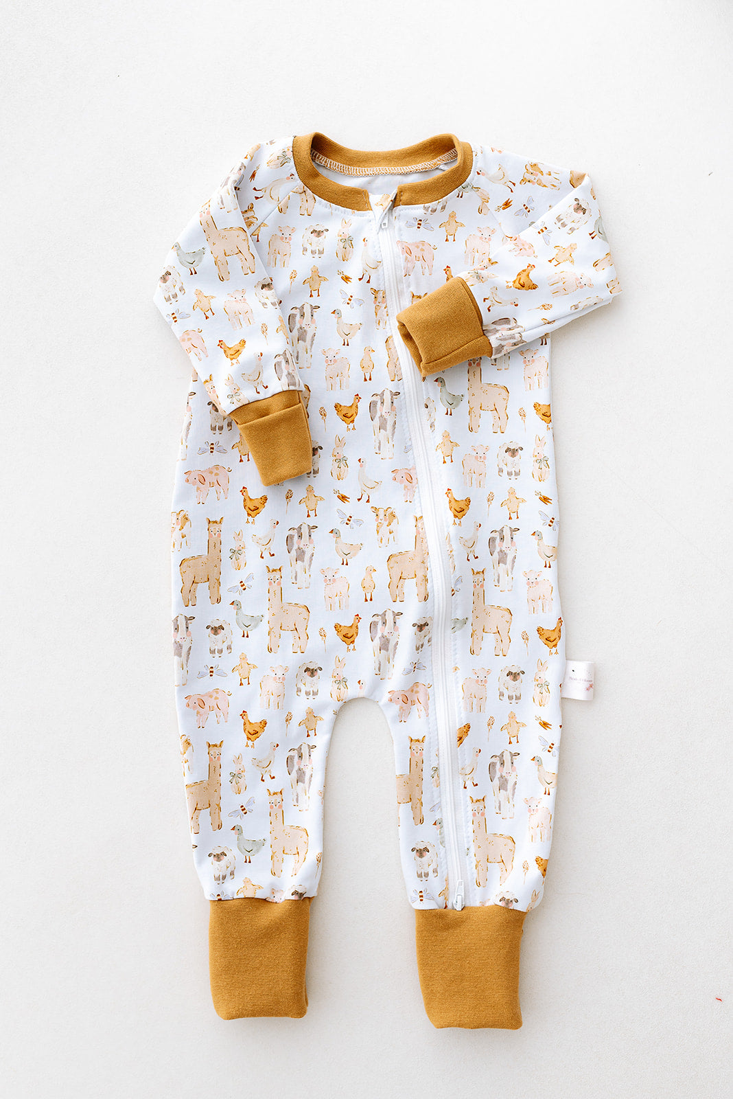 Image shows a handmade double zip baby sleepsuit in a neutral farm animal print on a white background with colour matching foldover hand and foot cuffs