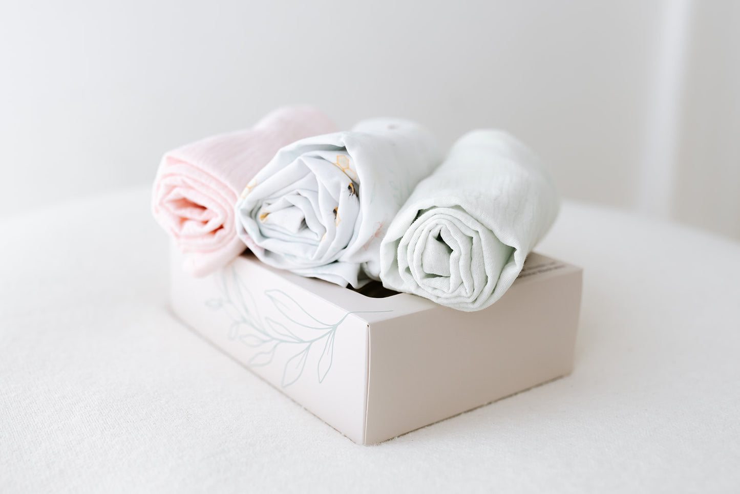 Three rolled-up muslins in pink, white, and mint on our Nestle and Bloom bespoke gift boxes