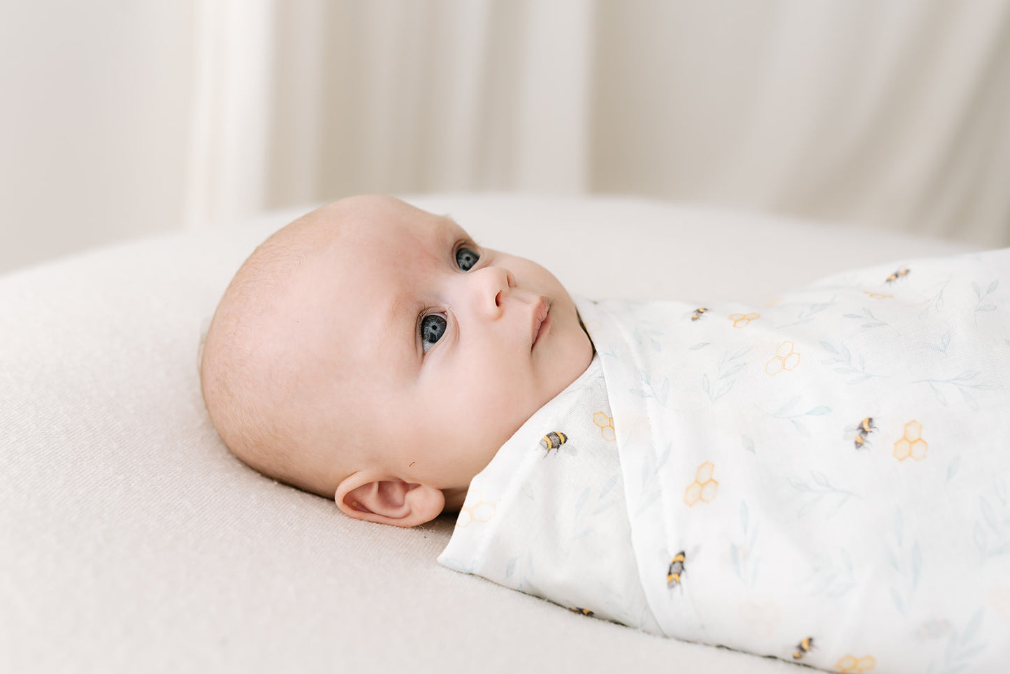 Baby swaddled in an organic muslin in our exclusive bee print on a light background displaying their versatile use